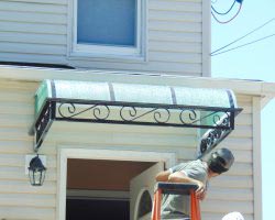 A man on a ladder working on the awning of a house.